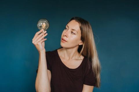 Girl turning head almost sideways to look at a light bulb she's holding up