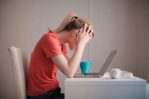 Side view of female seated with head in hands looking at laptop